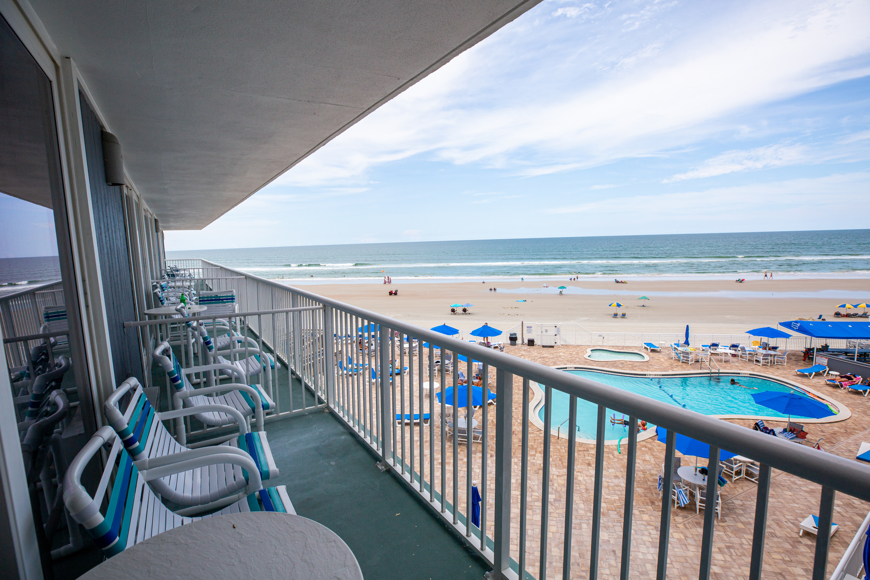 A beachfront balcony with a view of the ocean and pool area.