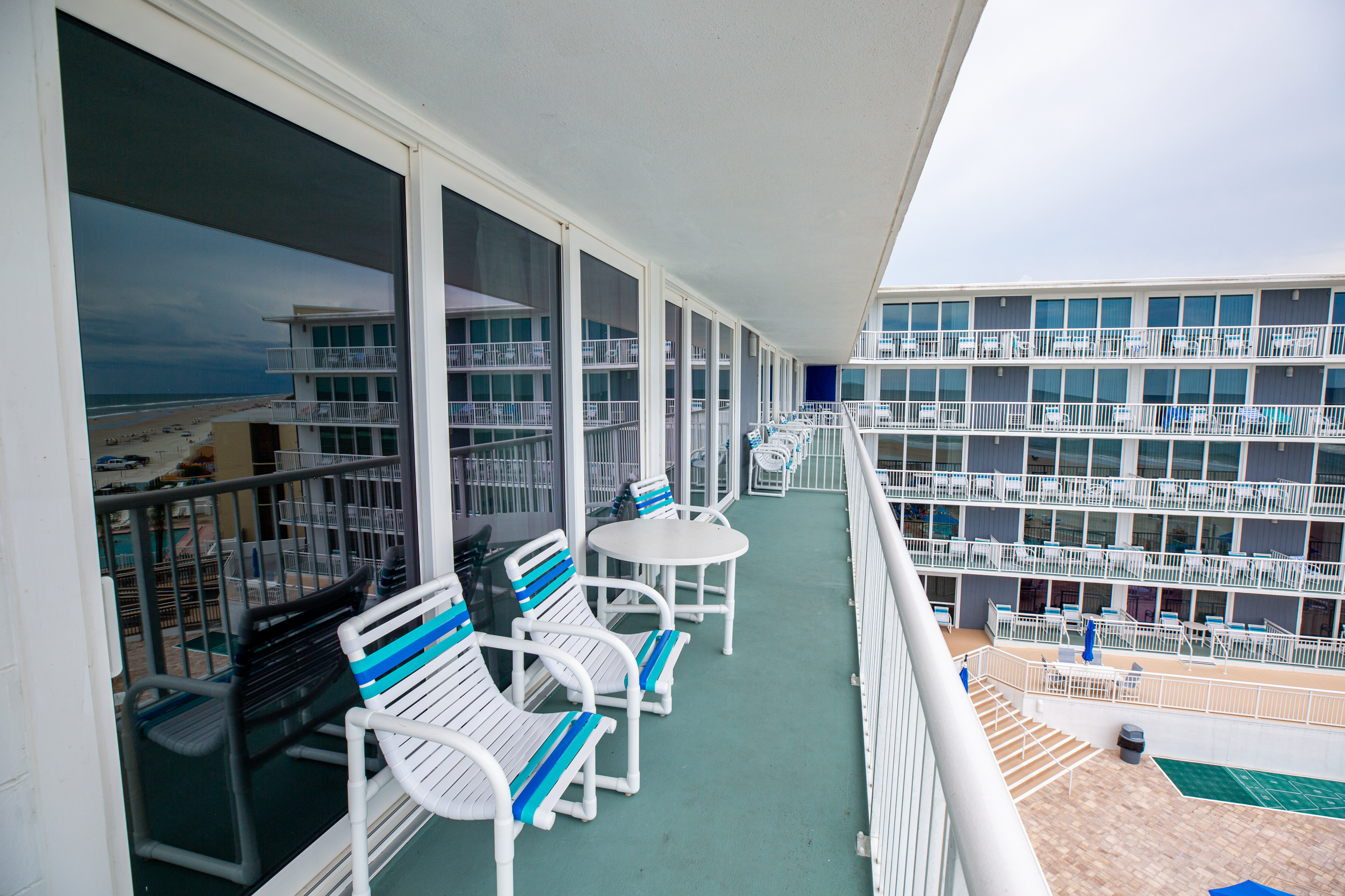 A balcony with white railing and blue accents overlooking the ocean and pool area.