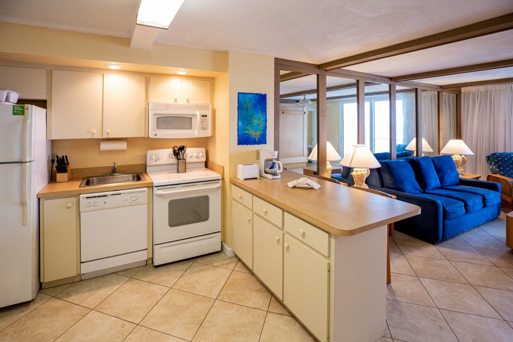 A kitchen with white appliances and a living area with a blue couch.